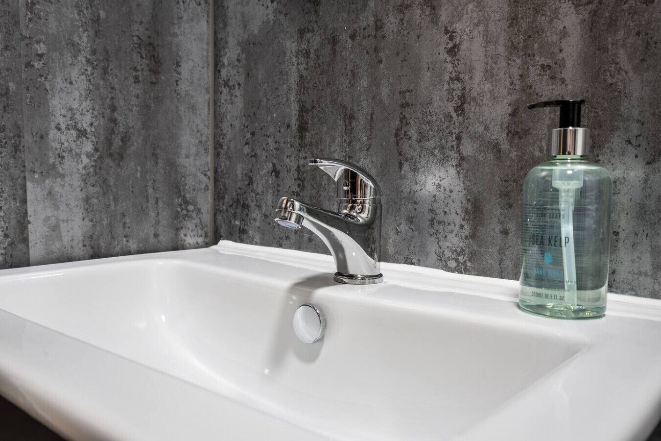 A white bathroom sink with a modern chrome faucet and a clear glass bottle of hand soap.