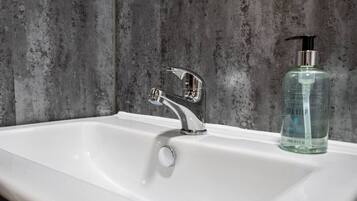 A white bathroom sink with a modern chrome faucet and a clear glass bottle of hand soap.