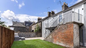 A residential property with a well-maintained lawn, a brick staircase leading to a balcony, and a wooden fence.