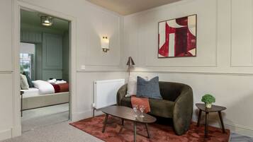 A modern living room with a green sofa, a coffee table, and a red rug. There is a painting on the wall and a small plant on a side table.