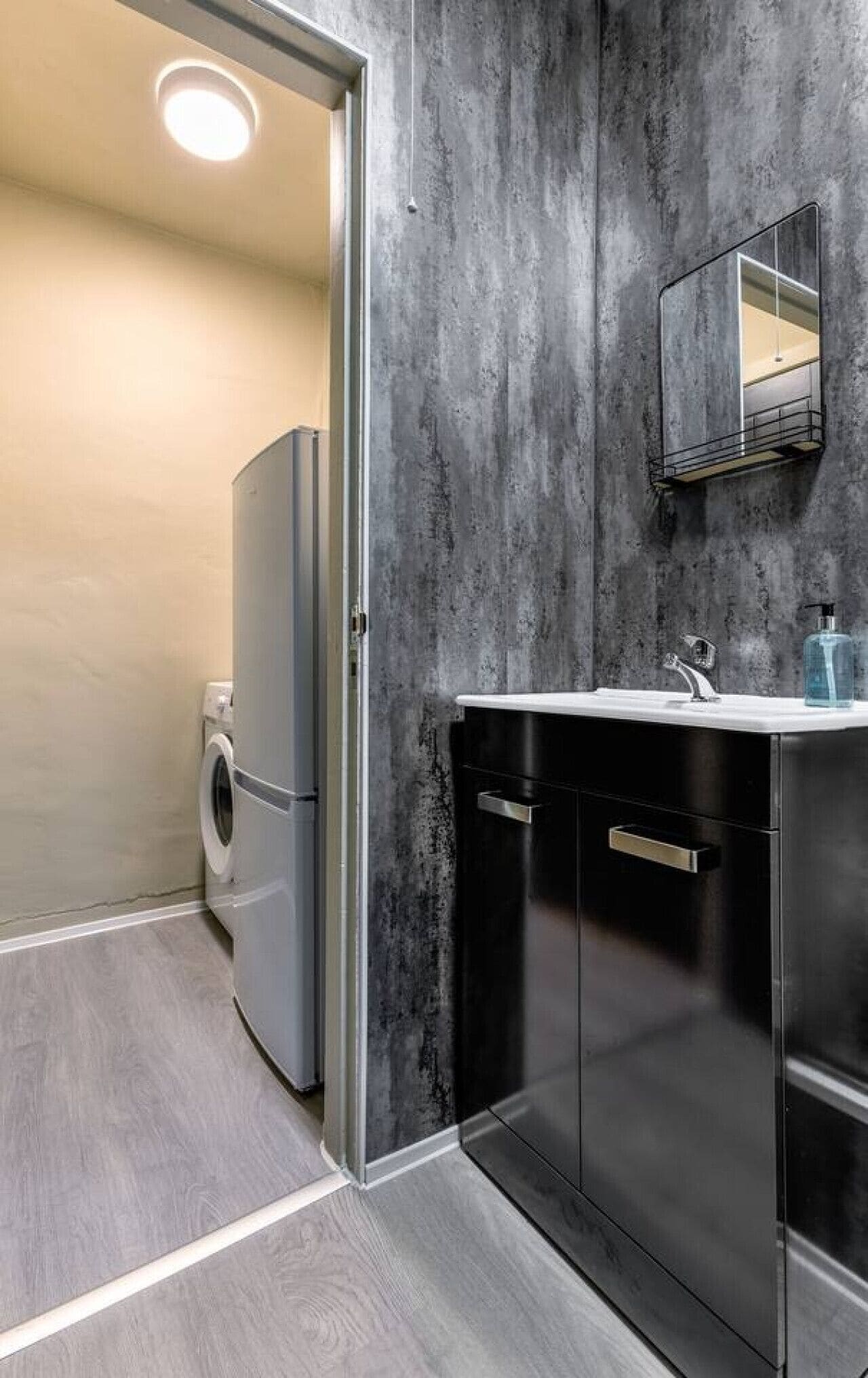 Een moderne badkamer met een grijze marmeren wand, een inbouwwastafel met spiegel, en een wasmachine.