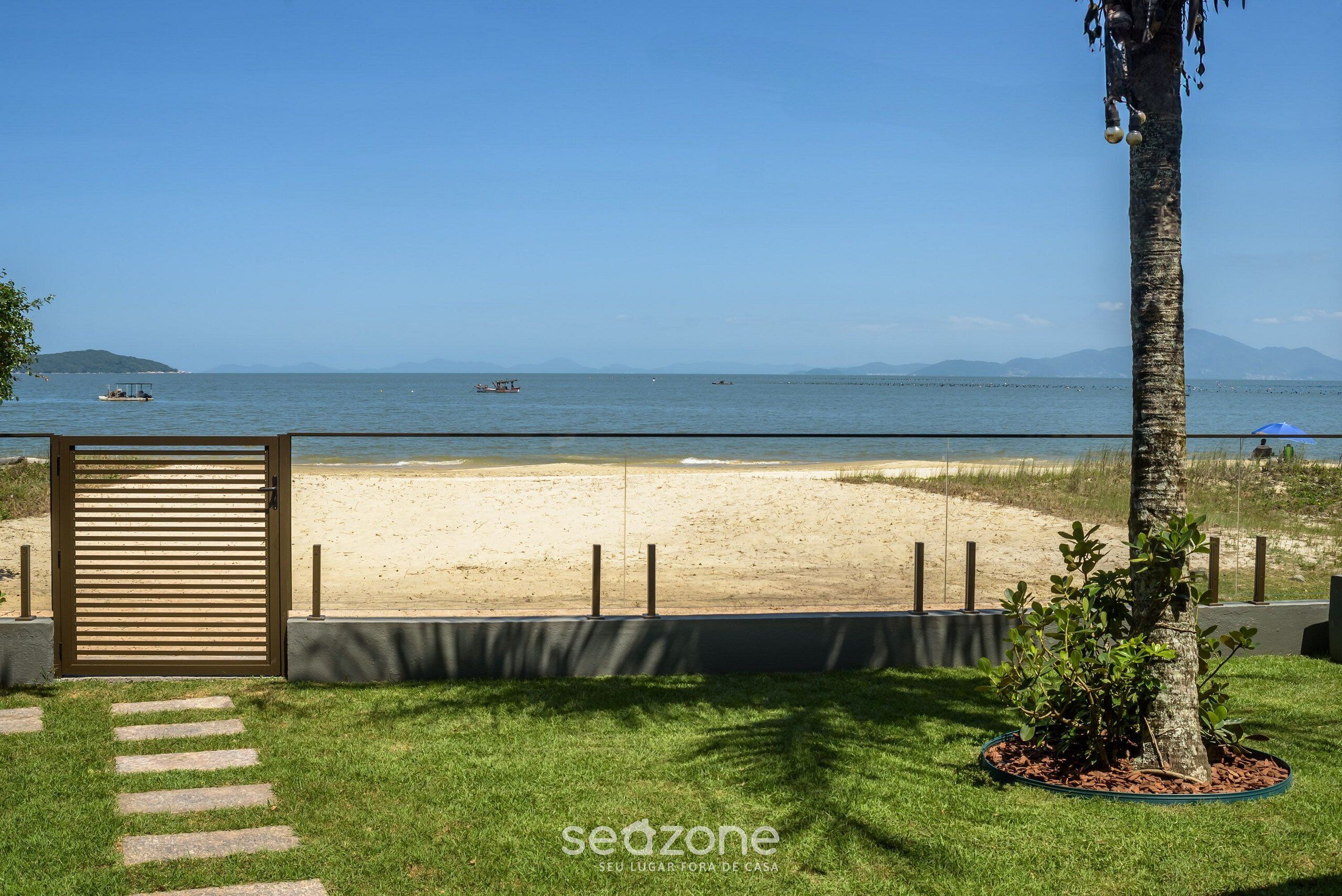 Een strandzicht met een palmboom, een poort en een pad naar het strand.