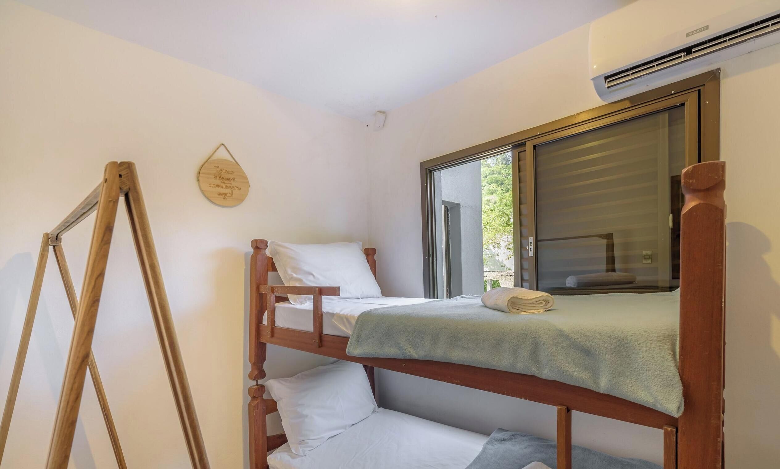 Una habitación pequeña con cama individual, una escalera de madera, una ventana con persianas y un aire acondicionado de pared.