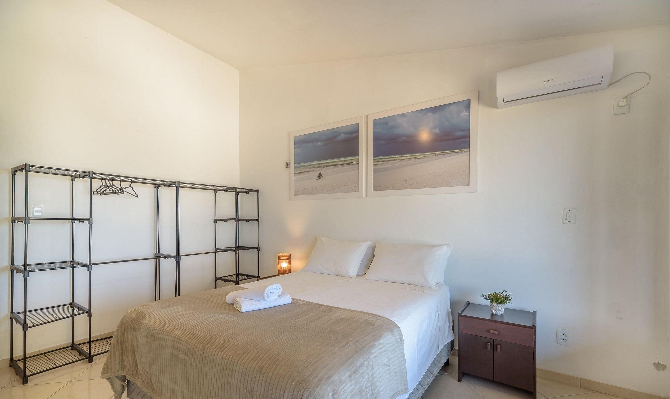 Ein Schlafzimmer mit einem Bett, einem Metallschrank, einem Nachttisch mit Lampe und einer Wand-Klimaanlage.