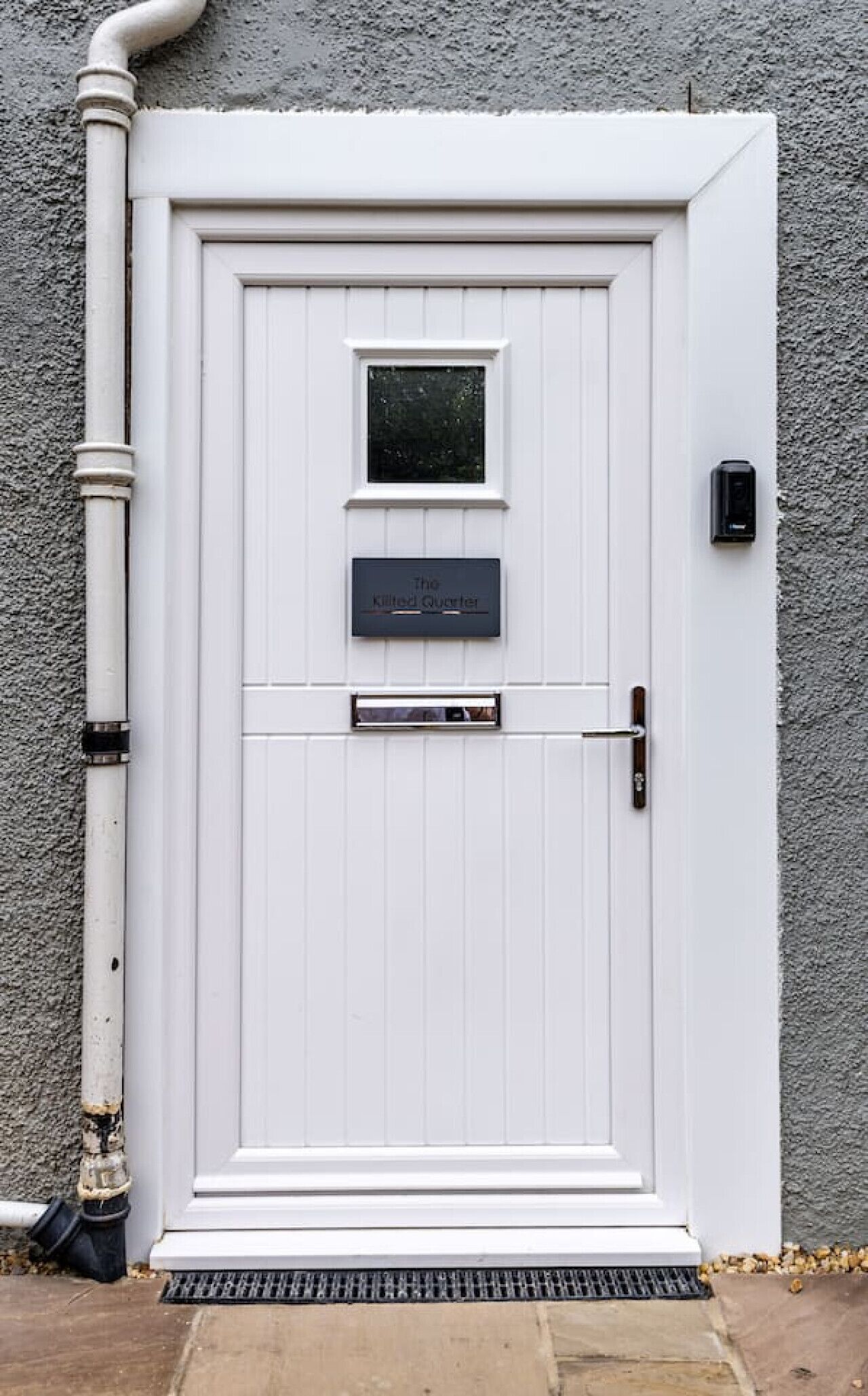 Une porte d’entrée blanche avec une petite fenêtre, une fente pour le courrier et un interphone.