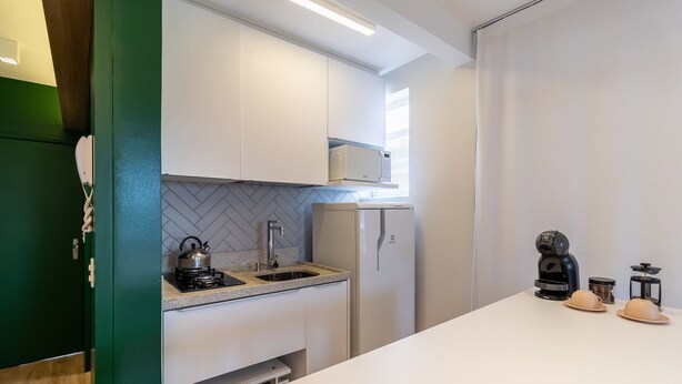 A modern kitchen with white cabinets, a microwave, a refrigerator, a kettle, and a coffee machine. - Charming Studio in Itacorubi Jvv303 (Florianópolis)