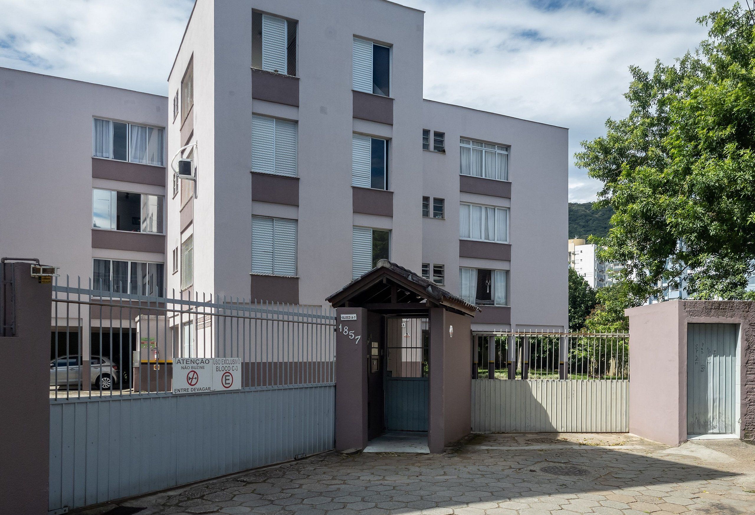 Un edificio residencial de varios pisos con entrada protegida por una reja, un pequeño porche cubierto y un camino de acceso pavimentado.
