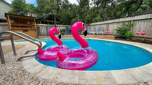 Ein Swimmingpool mit rosa Flamingo-Schwimmfiguren und einer Holzterrasse mit einer Bar.