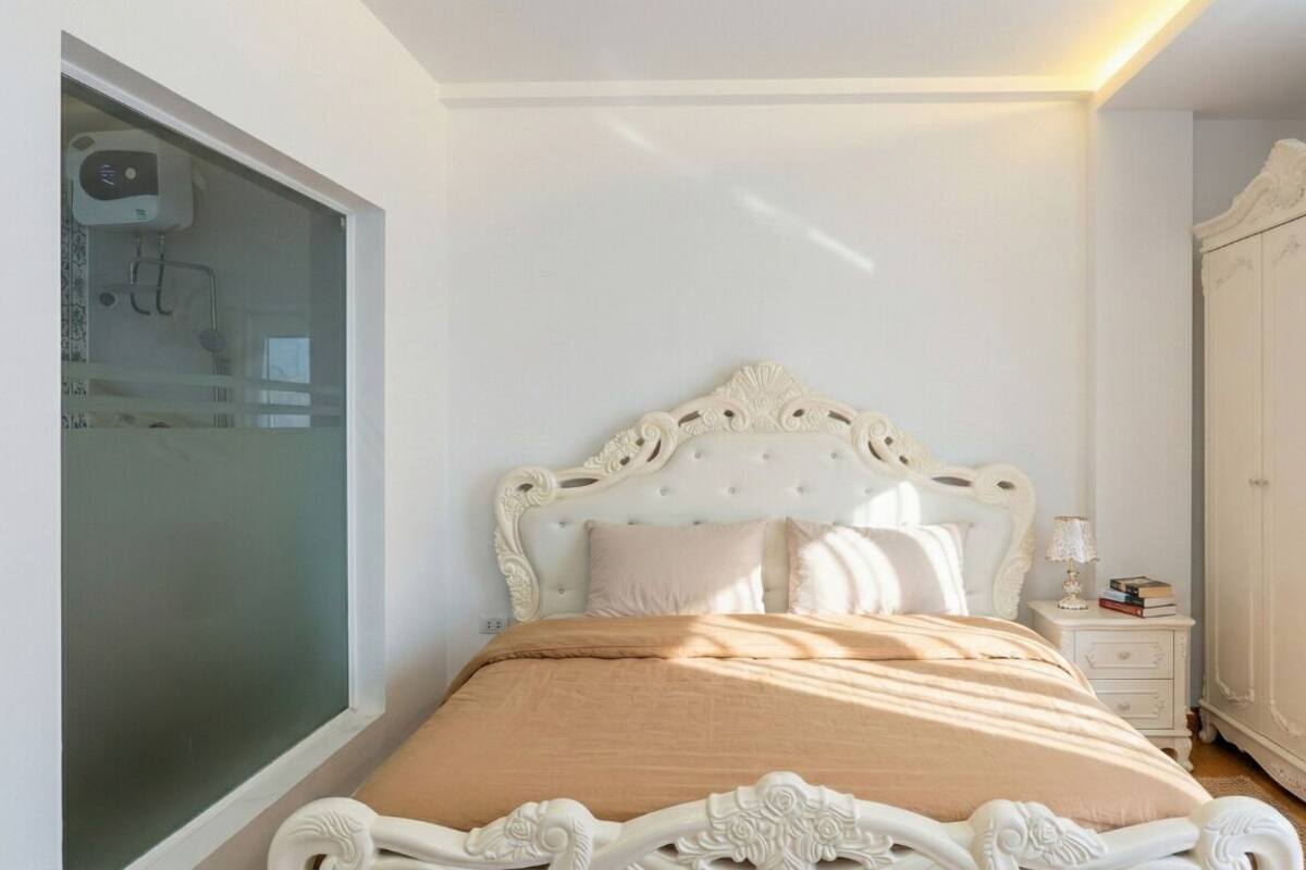 Un dormitorio con una cama blanca ornamentada, una mesita de noche con lámpara y un armario.