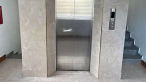 Un ascensor moderno con detalles metálicos, rodeado de paredes y suelos de mármol.
