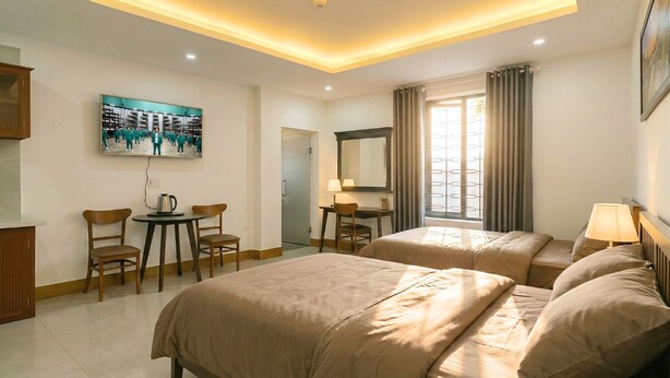 Habitación de hotel con dos camas, un escritorio, una silla, una mesa de centro, un televisor y una ventana con cortinas.
