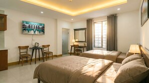 Habitación de hotel con dos camas, un escritorio, una silla, una mesa de centro, un televisor y una ventana con cortinas.