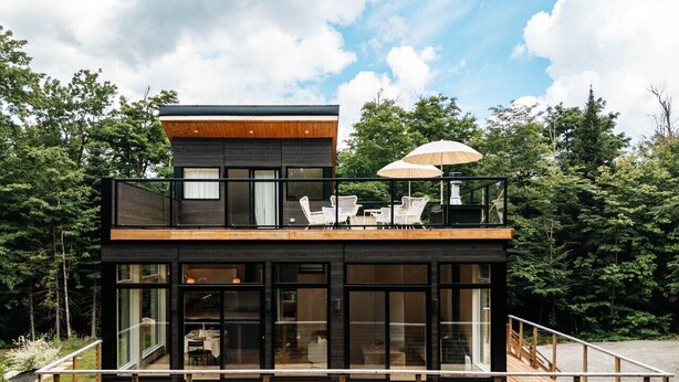 Una casa moderna de dos pisos con terraza de madera, ventanas amplias y mobiliario para exteriores.