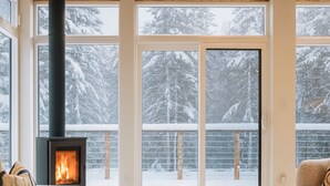 Una sala de estar moderna con una estufa de leña, ventanas amplias y vistas a árboles cubiertos de nieve.