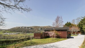 Une propriété rurale avec une allée de gravier menant à un bâtiment en bois, entourée de verdure et offrant une vue lointaine sur une falaise.