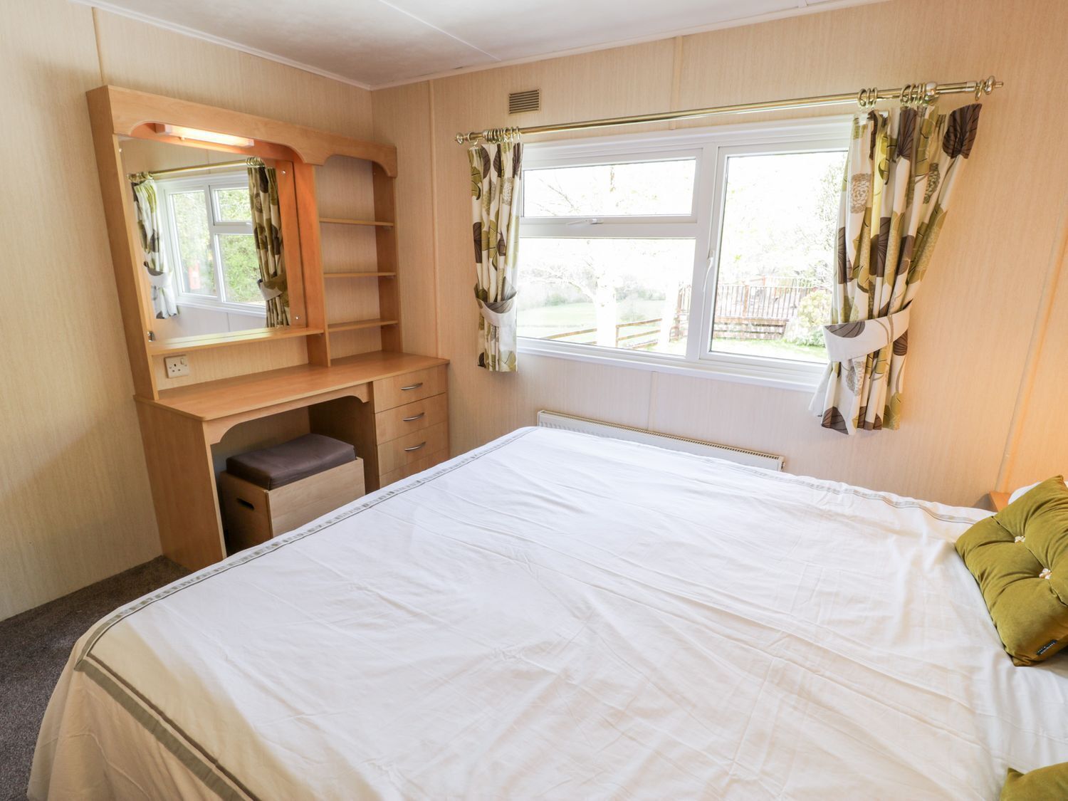 Une chambre à coucher avec un lit, un bureau, une chaise, un miroir et une fenêtre avec des rideaux.