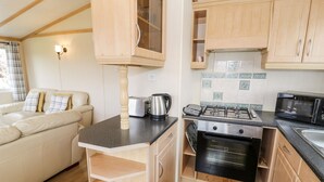 Une cuisine compacte équipée d’une cuisinière, d’un four à micro-ondes et d’un grille-pain. On y trouve un meuble en bois avec une porte en verre et un petit plan de travail.