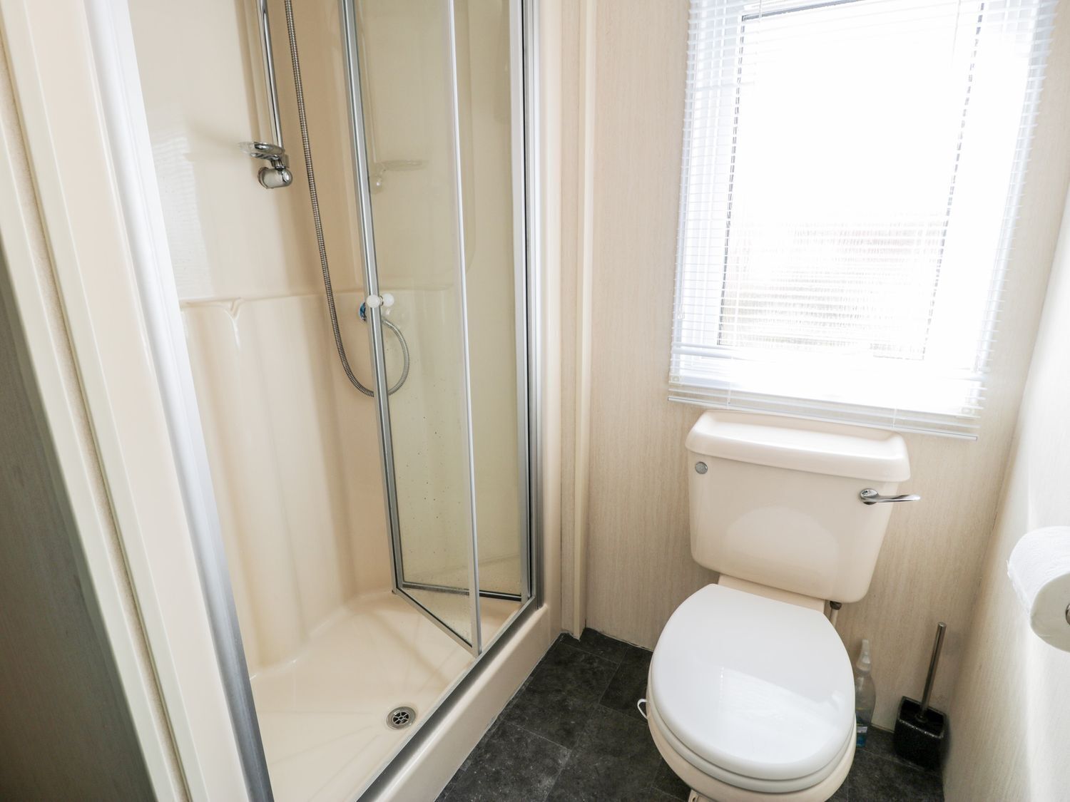 Un bagno con doccia vetrata, un water e una finestra con persiane.