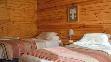 Una habitación con paredes de madera, dos camas con sábanas blancas, una mesita de noche con lámpara y una obra de arte enmarcada en la pared.
