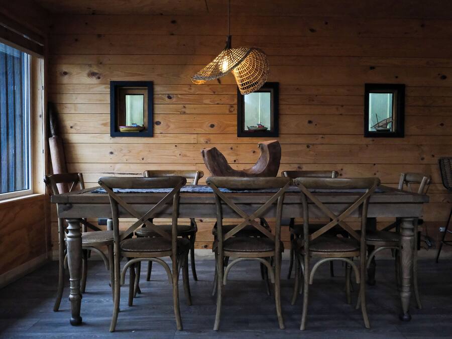 Un interior de madera con una mesa y sillas de comedor, cuadros en la pared y una lámpara colgante.