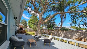 Eine überdachte Terrasse im Freien mit Korbmöbeln und einem Holztisch, umgeben von einem Holzzaun und Bäumen.