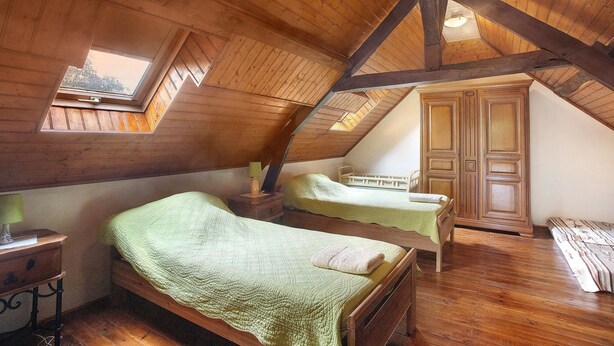Une chambre avec deux lits, des poutres apparentes, une lucarne et une armoire.