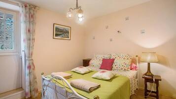 A bedroom with a bed, a bedside table, a lamp, a window with curtains, and a wall-mounted picture.