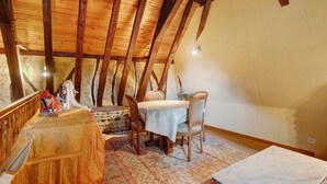 Un espace repas comprenant une table et des chaises, des poutres en bois et un mur en pierre.