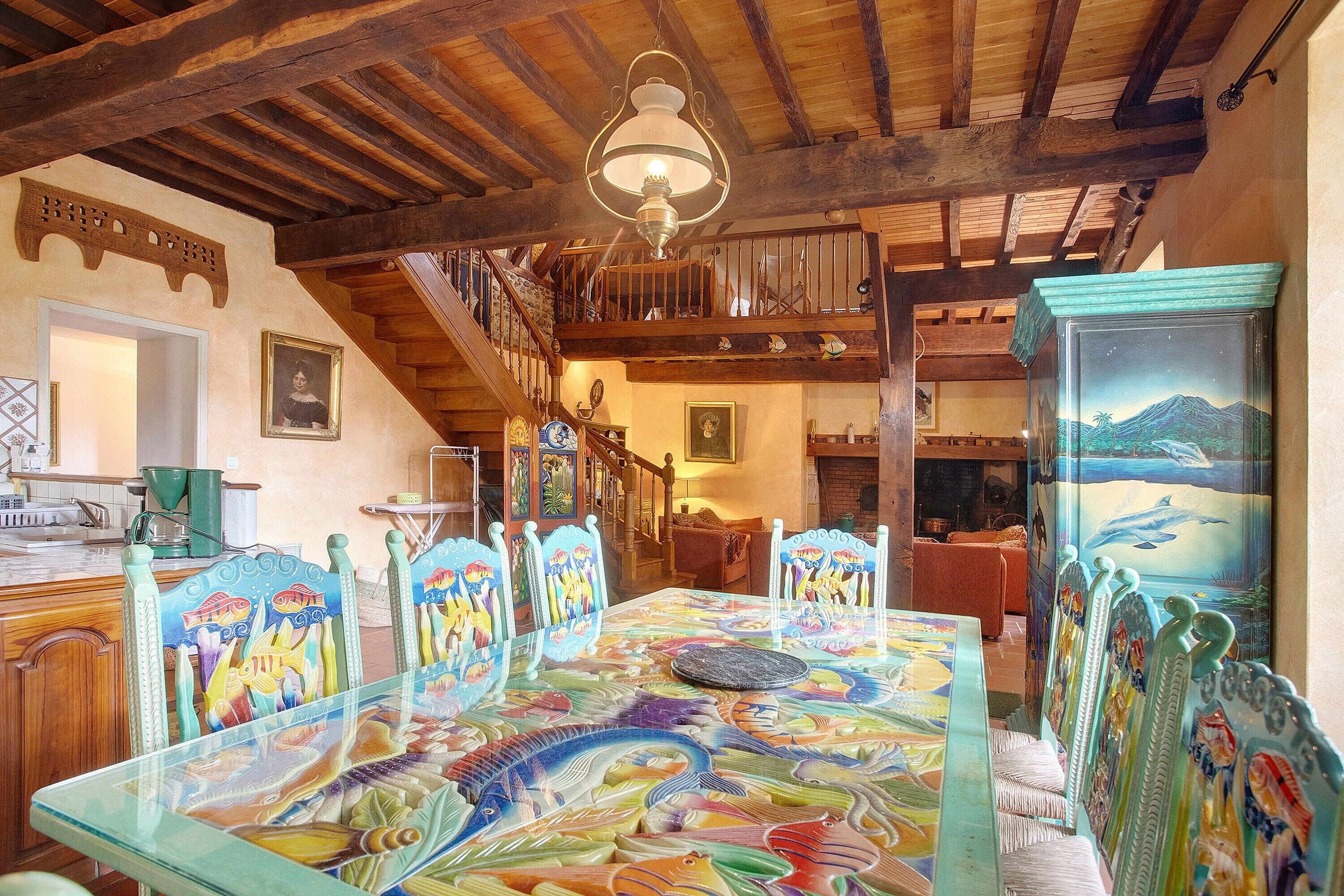 Un espace repas avec une table en verre, des chaises en bois et un escalier menant à un niveau supérieur.