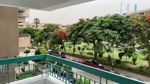 A balcony with a view of a residential street, parked cars, and lush greenery.