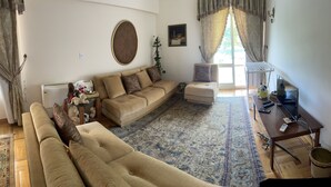 A living room with a beige sofa, a smaller sofa, a coffee table, and a TV stand with a TV and remote controls.
