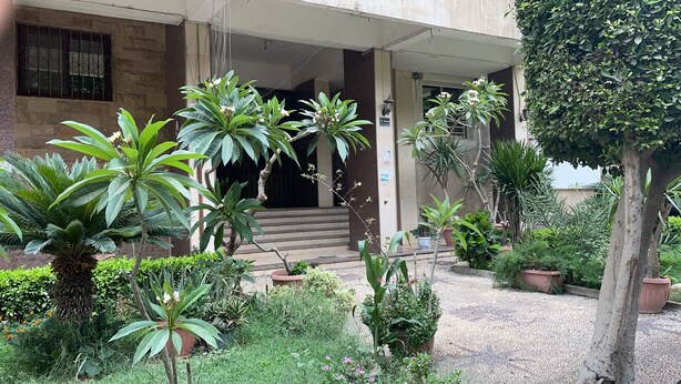 A building with a covered entrance, steps leading to a door, and various potted plants and greenery around the entrance area.