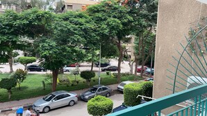 A residential area with parked cars, trees, and a building with a beige facade.