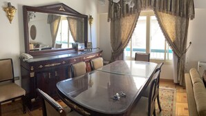 A dining area with a glass table, chairs, a wooden cabinet with a telephone, and a large mirror.