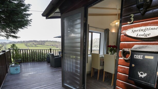 A wooden deck with a glass door leading to a dining area with a view of the countryside. - Springtime Lodge (Abergele)