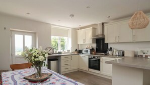 A modern kitchen with white cabinets, a central island, and a dining area with a patterned tablecloth. - St Gregorys Cottage (York)