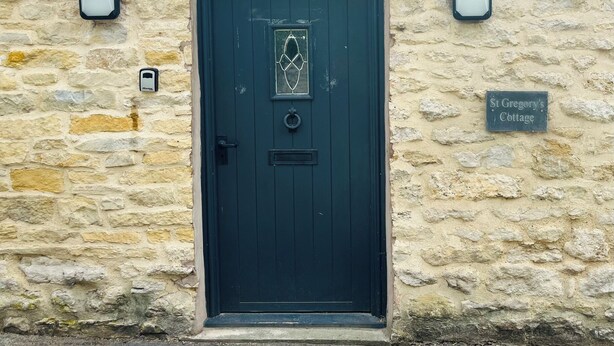 A dark green door with a glass panel and a knocker, set in a stone wall with a sign reading "St Gregory's Cottage". - St Gregorys Cottage (York)