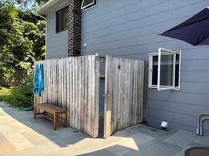 A wooden partitioned outdoor area with a bench, a window, and a hose.