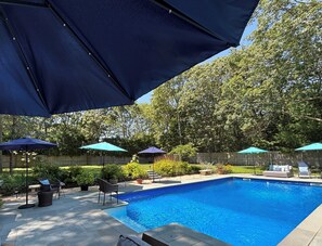 Una piscina con un borde de baldosas, rodeada de mobiliario exterior y sombrillas.