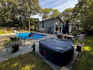A backyard with a swimming pool, outdoor furniture, and a covered hot tub.