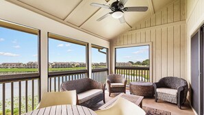 A balcony with wicker furniture, a ceiling fan, and a view of a golf course and buildings. - Boardwalk Villas 298 - Community Pool, Lake Front, Great Amenities + Dining! (Miramar Beach)