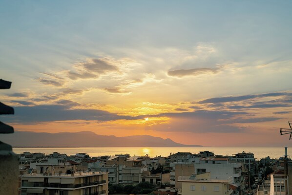A coastal cityscape at sunset with buildings and a clear view of the sea.