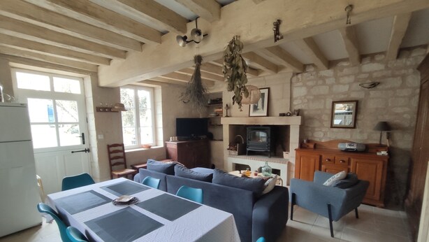 A cozy living room with a fireplace, a dining area with a table and chairs, and a kitchen area with a stove. - La petite massonnière (Beaumont-en-Véron)