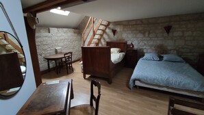 A bedroom with a wooden bed, a small table, a chair, a wooden desk, and a staircase leading to an upper level. - La petite massonnière (Beaumont-en-Véron)