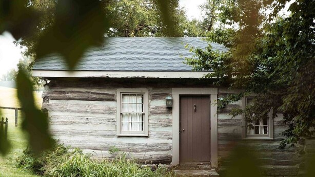 A rustic log cabin with a wooden door and a window, surrounded by greenery. - 1791 Cabin on Historic Horse Farm (Bourbon County)