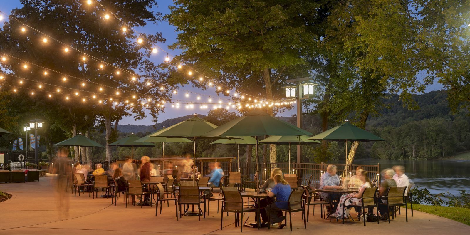 Un espace extérieur aménagé pour les repas, avec des guirlandes lumineuses, des parasols et des tables.