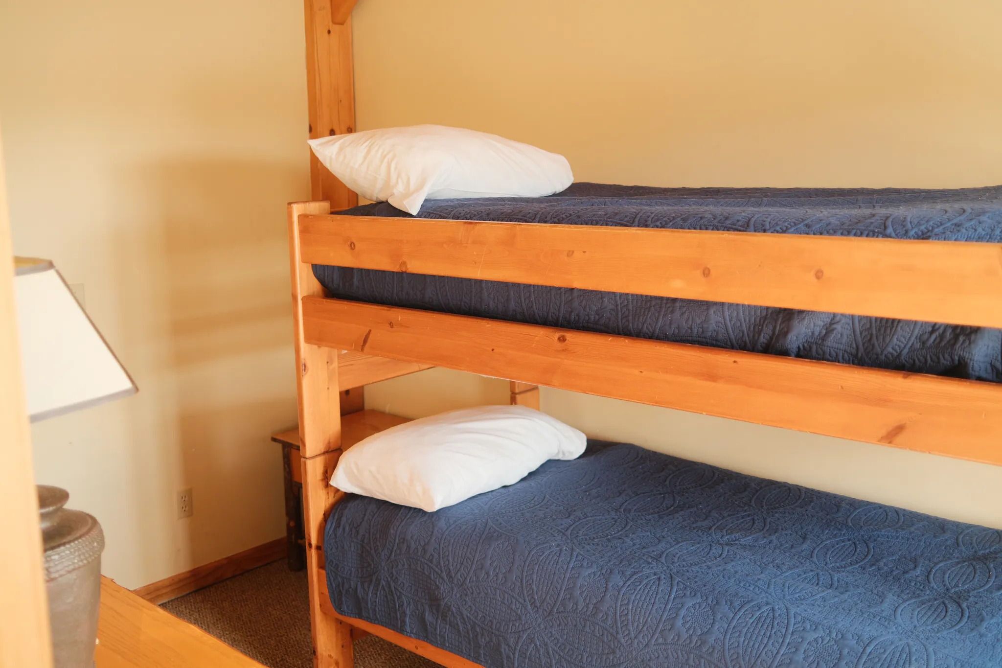 A bunk bed with two levels, each with a white pillow and a blue quilted mattress.