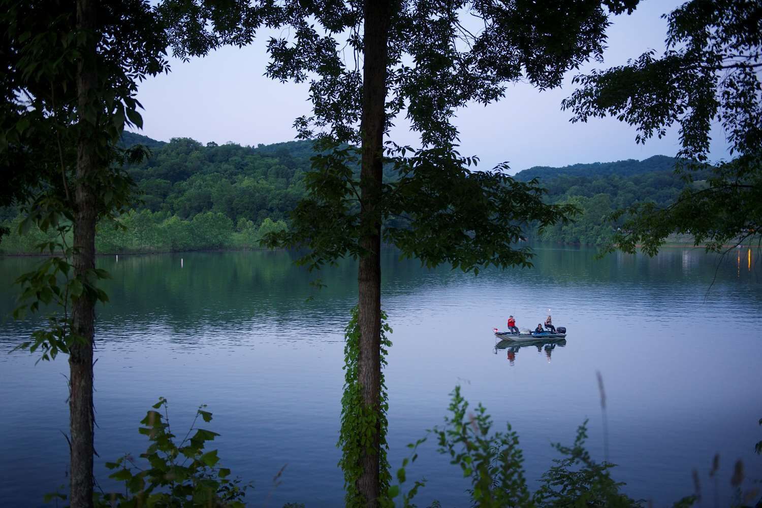 Un llac tranquil envoltat per un bosc dens amb una barca que transporta dues persones.