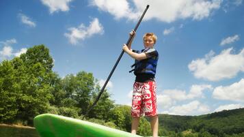 A person standing on a green paddleboard in a body of water with trees and hills in the background.