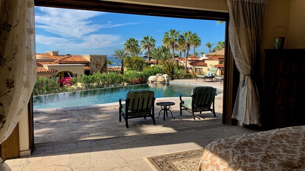 A room with a view of a pool, two lounge chairs, a small table, and a bed.